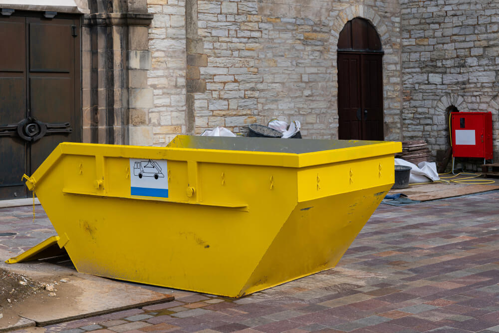 bright yellow skip bin positioned near stone building